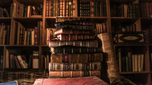Books piled on a brown wooden shelf